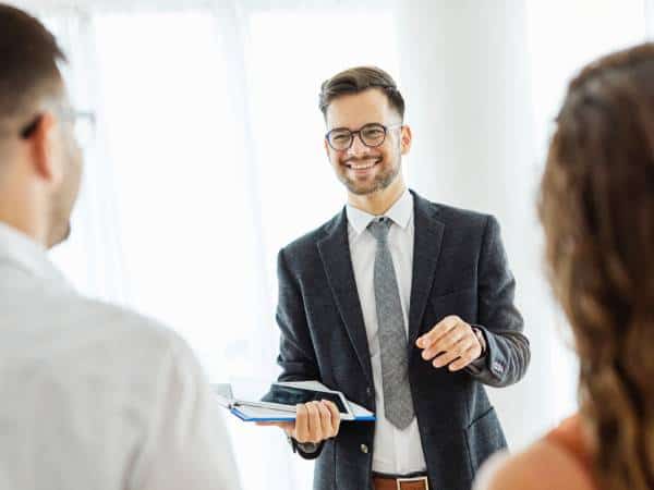 A smiling real estate agent in front of a couple of real estate buyers.