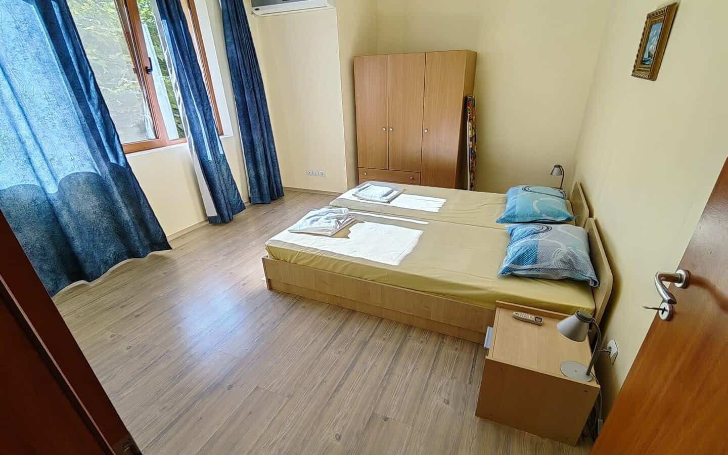 tristaen-apartament-prodajba-zlatni-pqsaci-3 Спалня с две единични легла и голям кафяв гардероб.