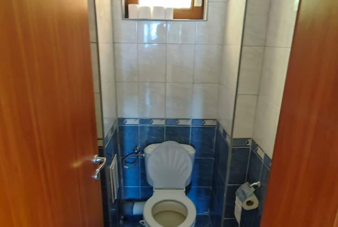 Тесен санитарен възел с тоалетна и малък прозорец.