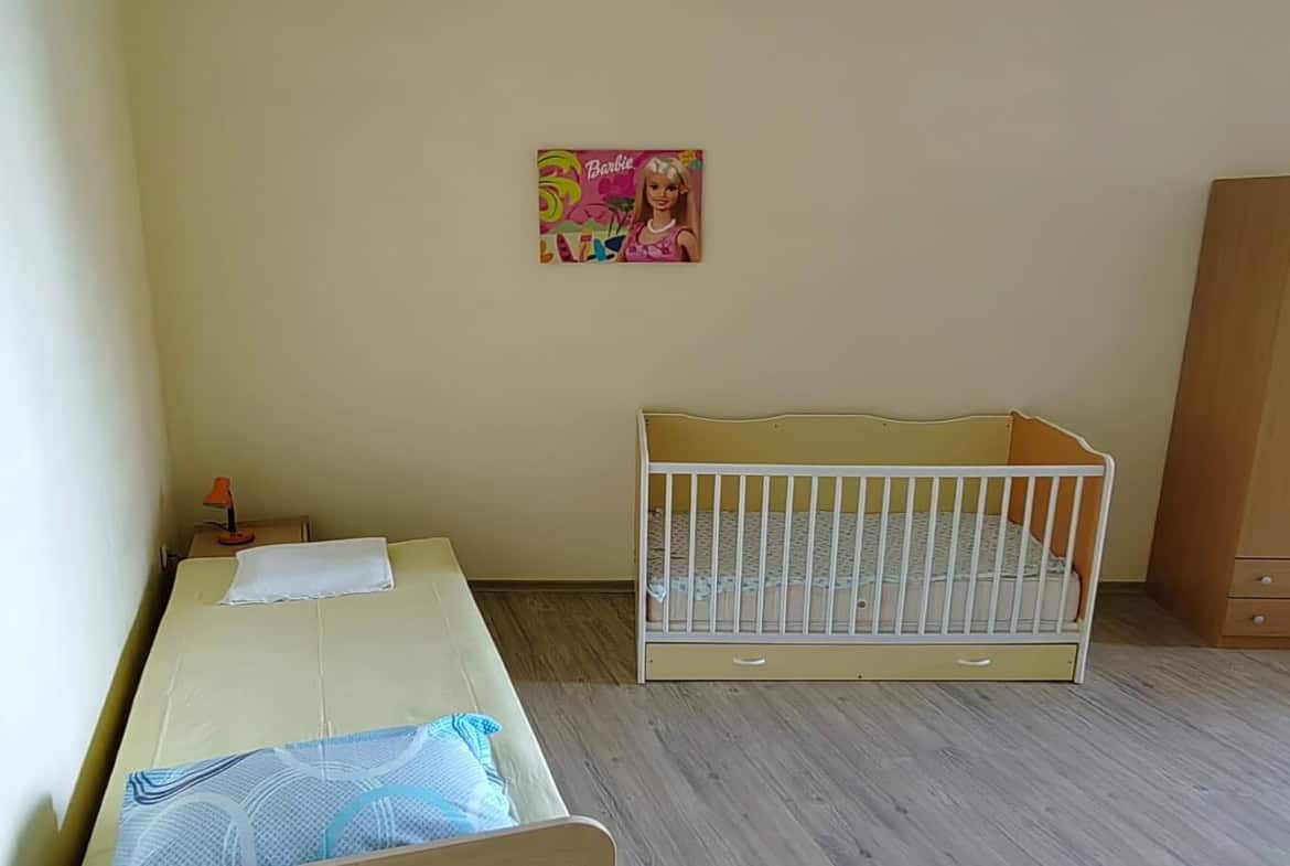 Спалня с детско креватче и плакат на Барби на стената.