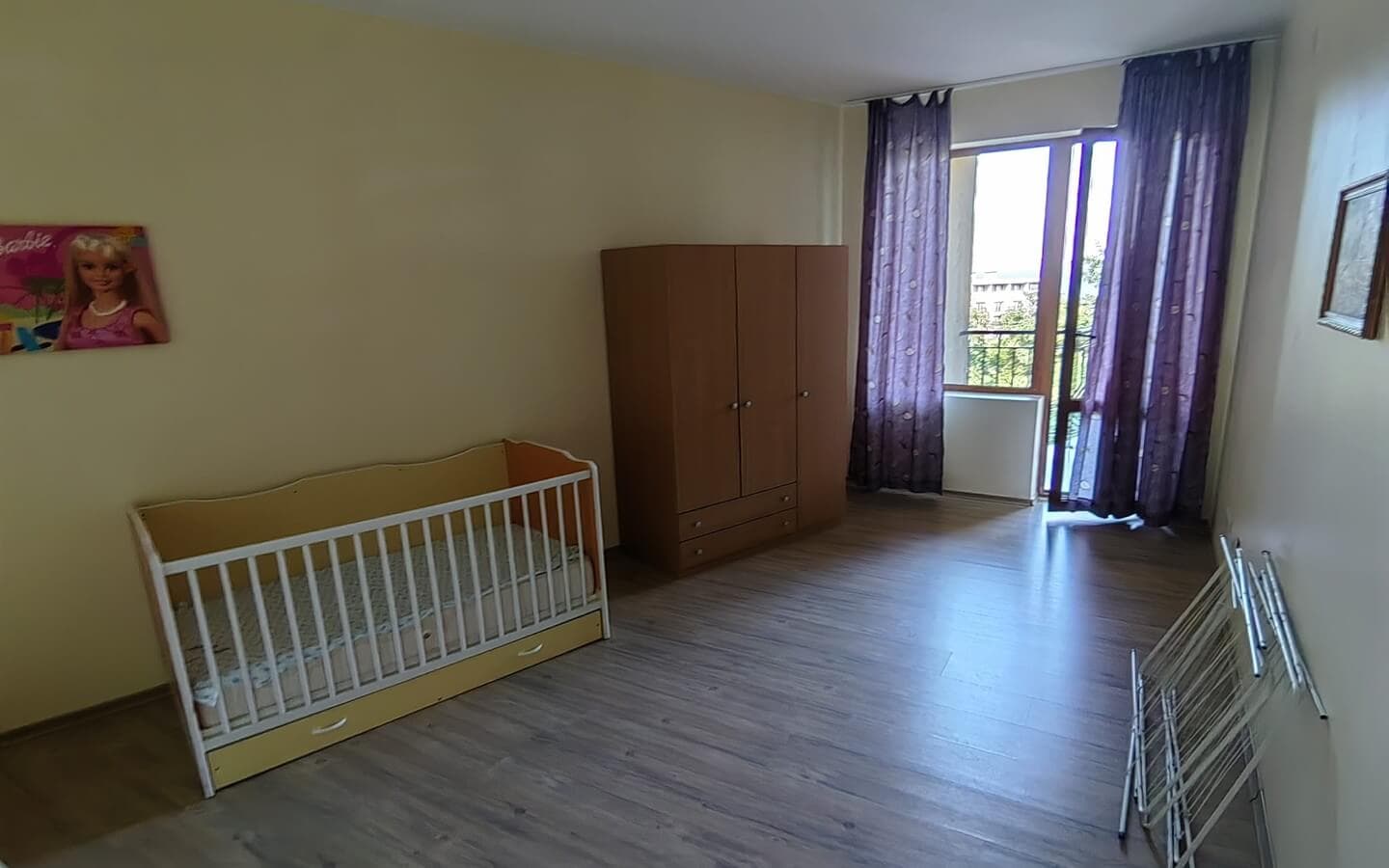 tristaen-apartament-prodajba-zlatni-pqsaci-9 Спалня с бебешко креватче, голям кафяв гардероб и изглед към балкон.