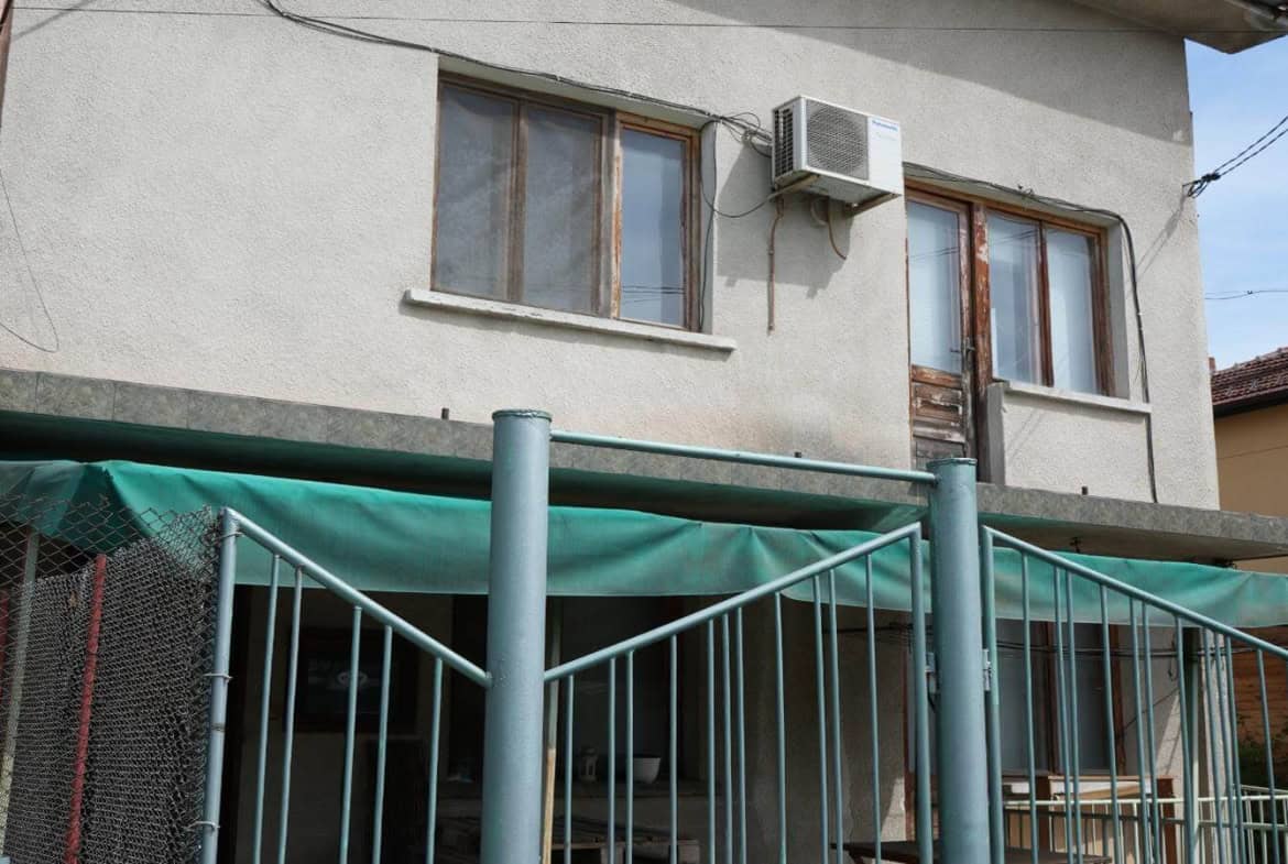 The front of the house overlooks a fenced entrance and green gates.
