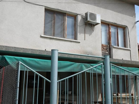 The front of the house overlooks a fenced entrance and green gates.