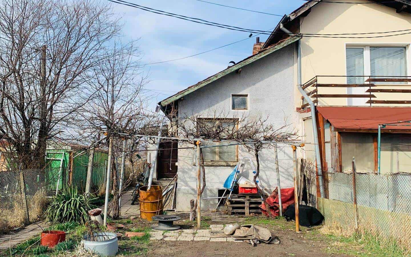 kushta-prodajba-kostinbrod-sofia-1 Къща с изглед към заден двор с ограда, множество дървета и външни съоръжения.