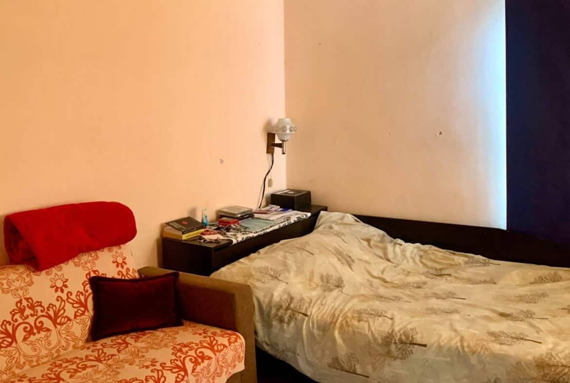 Спалня с розови стени, единично легло и малко червено диванче.