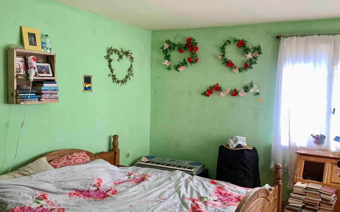 kushta-prodajba-kostinbrod-sofia-4 Спалня със зелени стени, декорирана с венци от изкуствени цветя и книги до леглото.