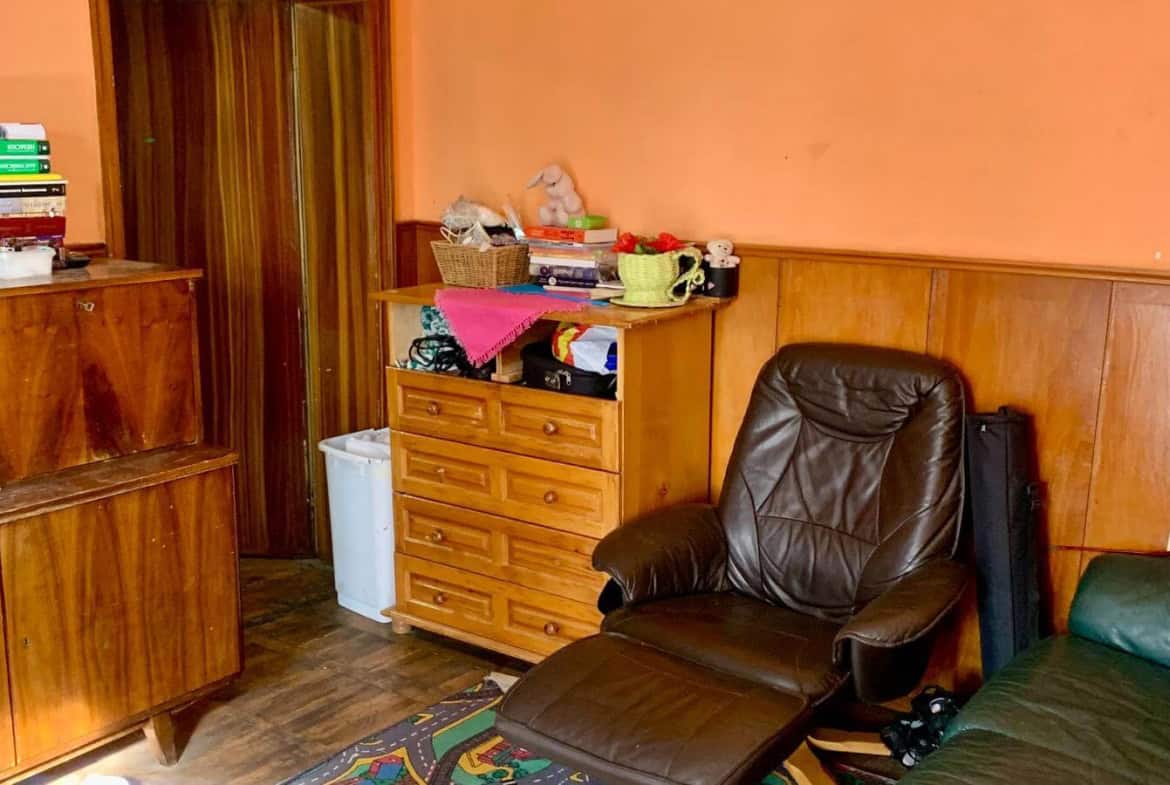 Стая с дървени мебели и червени стени, оборудвана с кожен стол и килими.