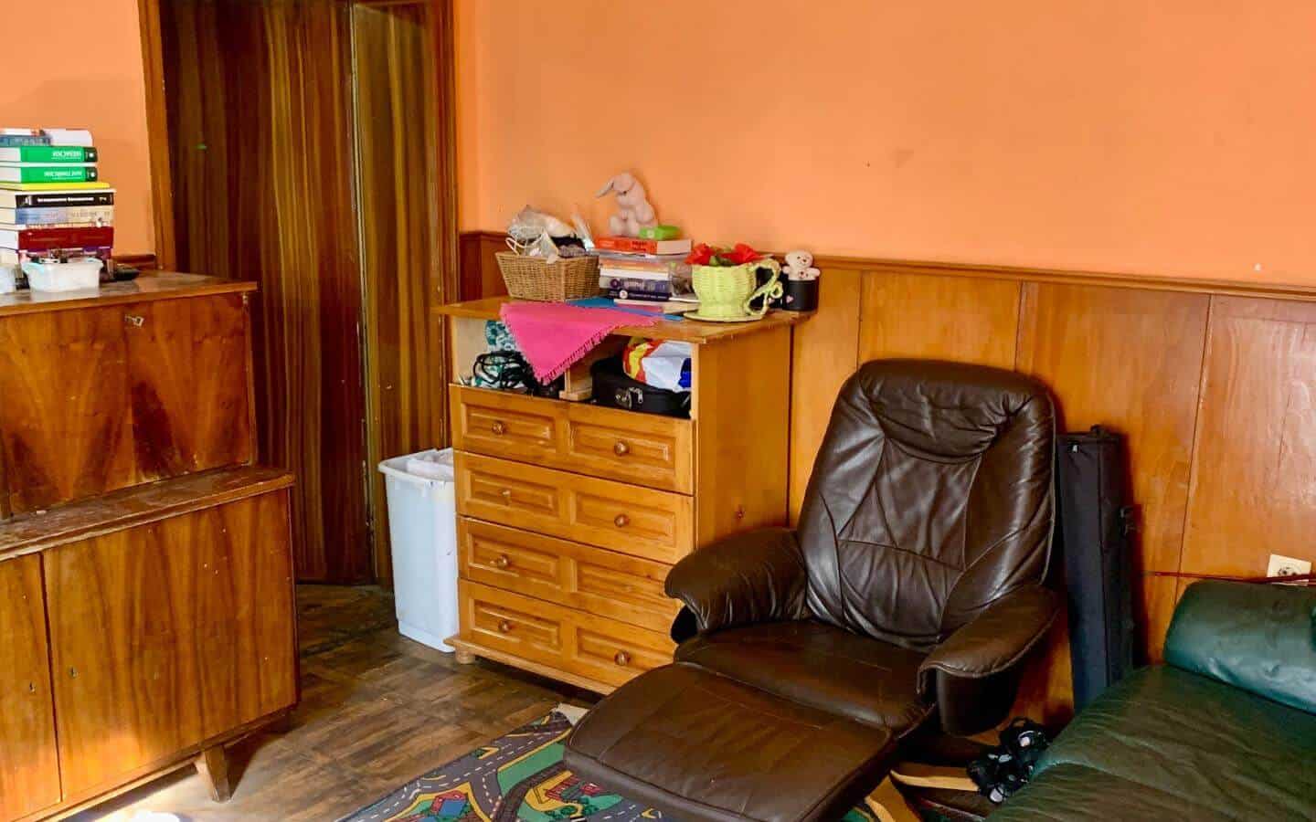 kushta-prodajba-kostinbrod-sofia-5 Стая с дървени мебели и червени стени, оборудвана с кожен стол и килими.