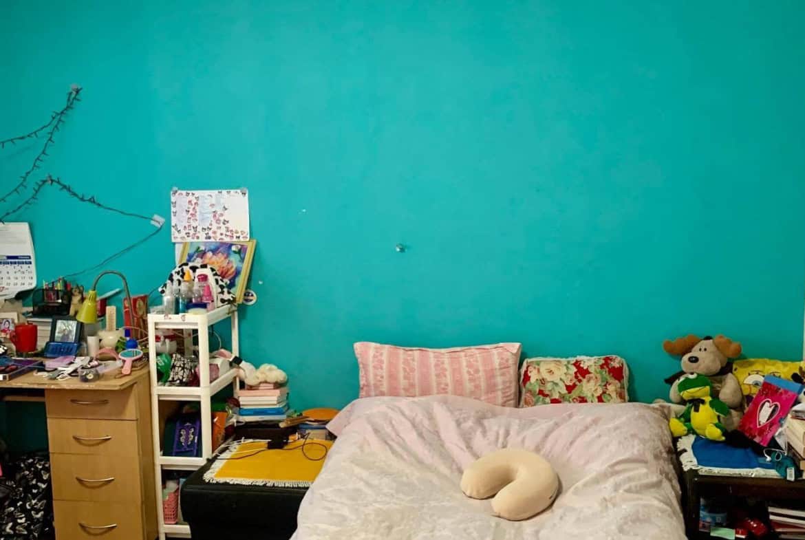 Спалня с тюркоазени стени, обилно украсена с играчки и лични вещи.