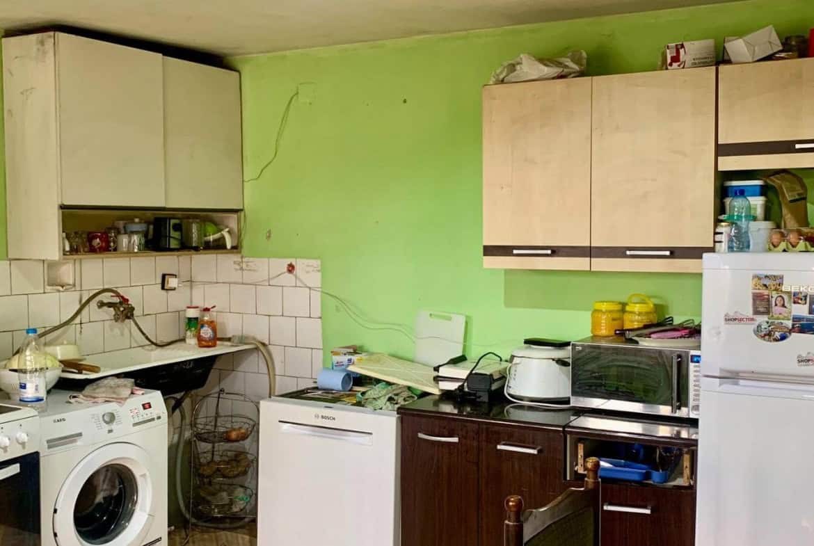 Кухня със светлозелени стени и различни кухненски уреди, включително пералня и хладилник.