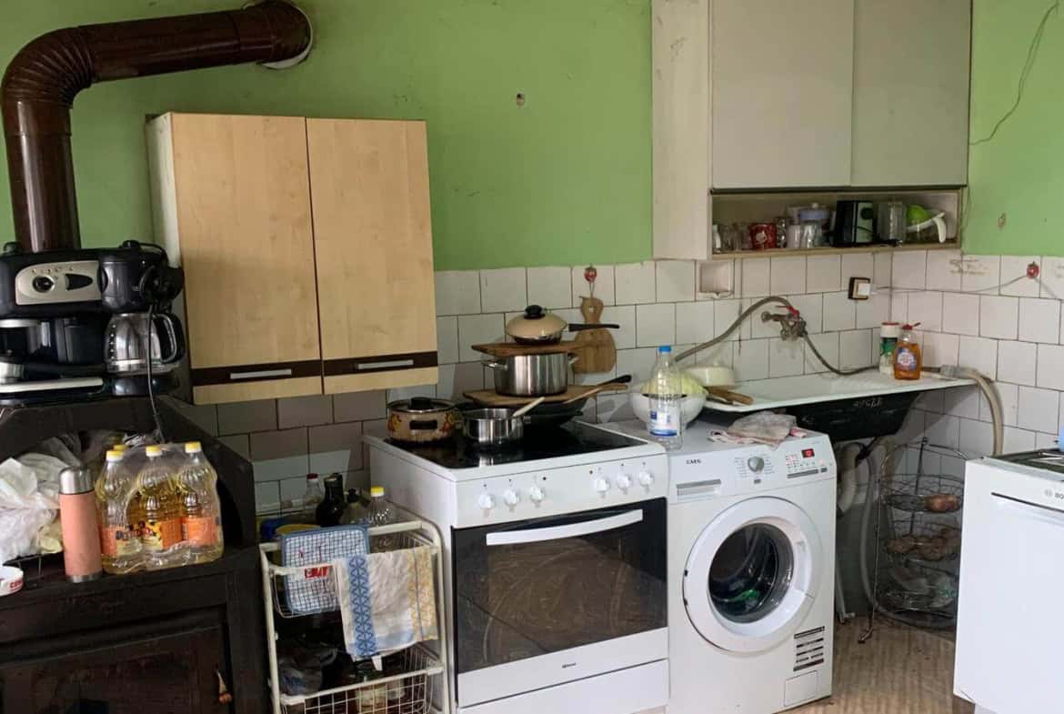 Кухня със светлозелени стени, оборудвана с готварска печка и дървена мебел.