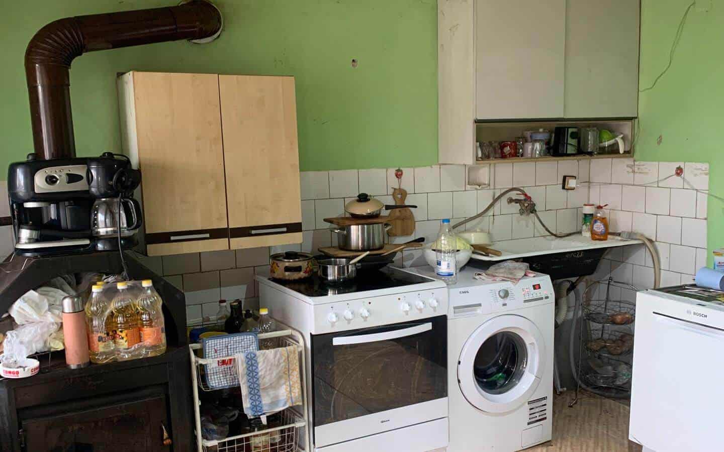 kushta-prodajba-kostinbrod-sofia-8 Кухня със светлозелени стени, оборудвана с готварска печка и дървена мебел.