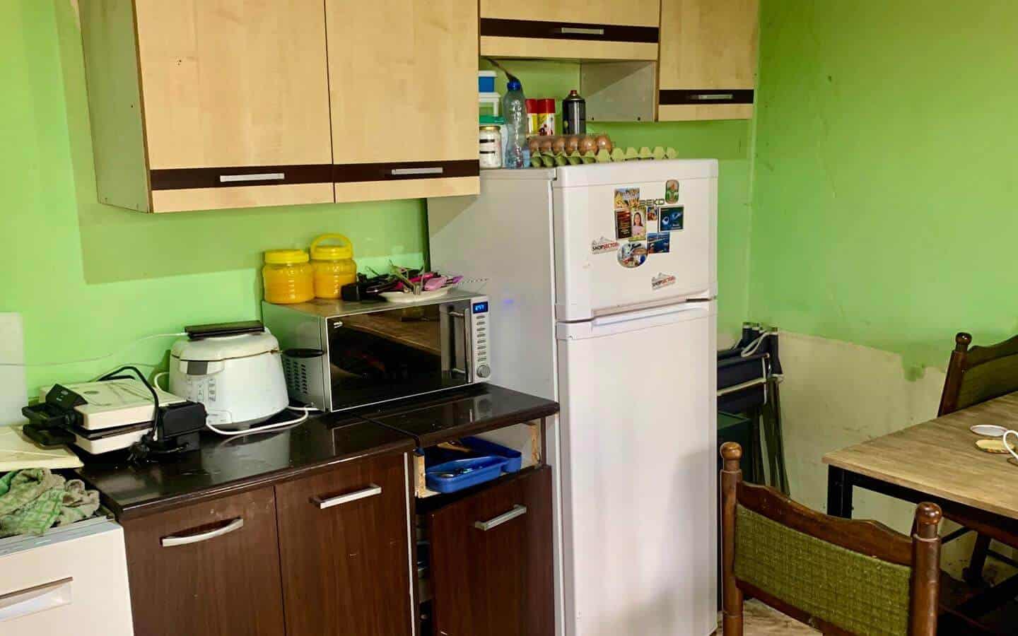 kushta-prodajba-kostinbrod-sofia-9 Друг ъгъл на кухнята с видим хладилник и малка трапезна маса.