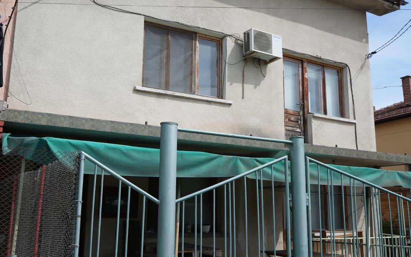 kushta-za-prodajba-kostenec-veranda-1 Предният двор на къщата с изглед към ограден вход и зелени врати.