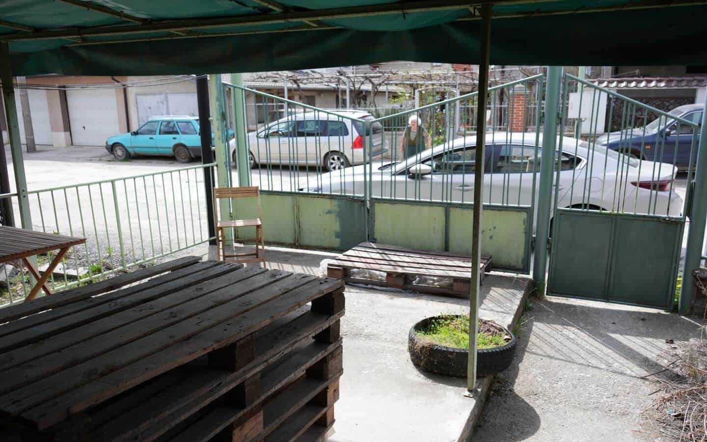 kushta-za-prodajba-kostenec-veranda-2 Веранда с дървени палети и стари столове, гледаща към улицата и паркирани автомобили.