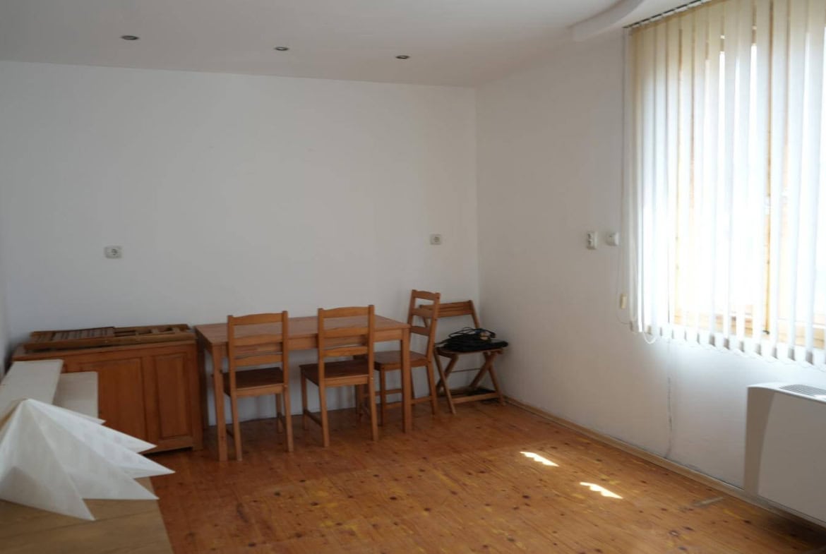 Просторна и светла всекидневна с дървен под, маса и столове.