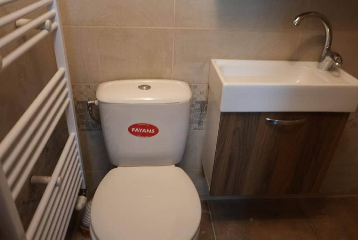 Баня с бял санитарен фаянс и дървени шкафчета.