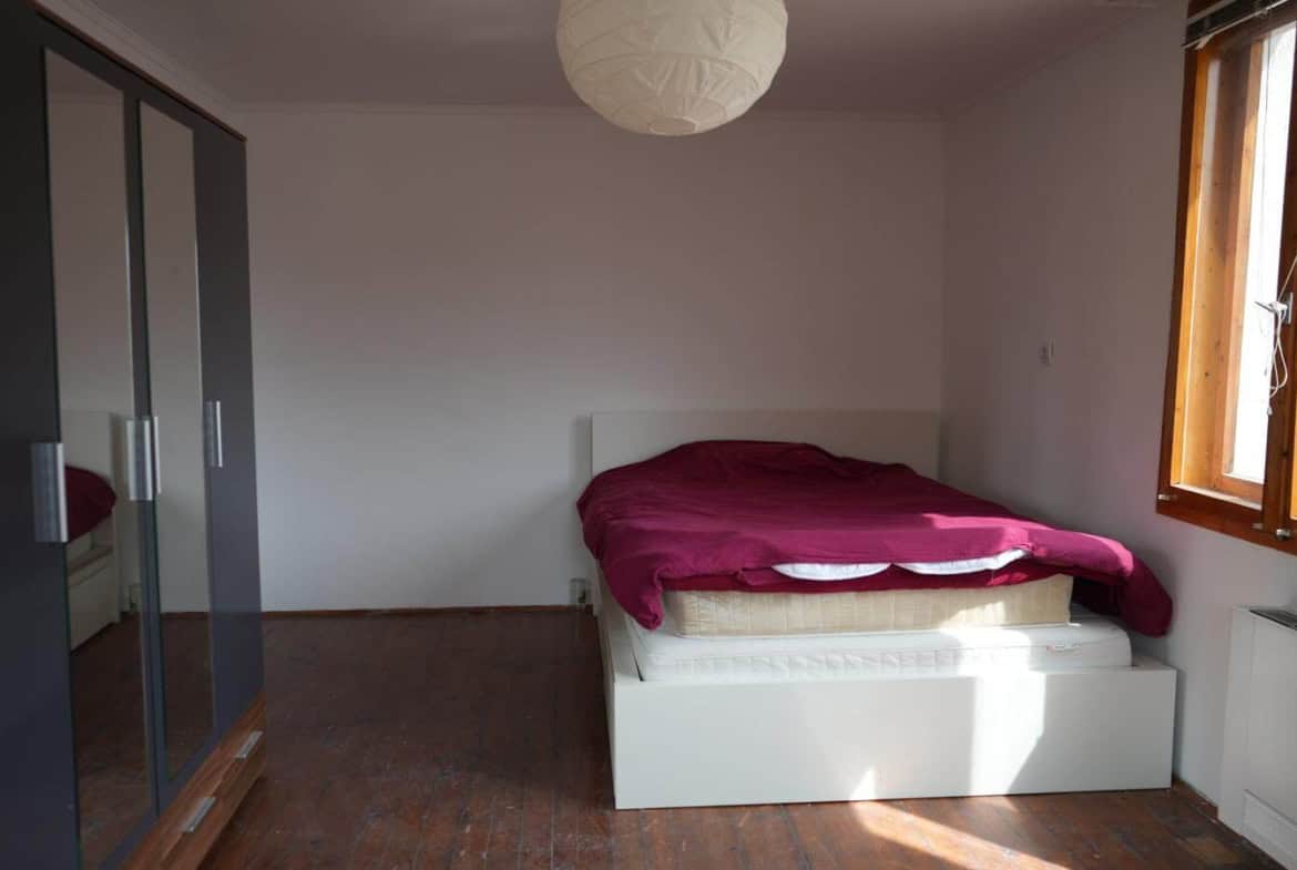 Спалня с двойно легло, облечено в тъмно червено чаршаф и голям гардероб.