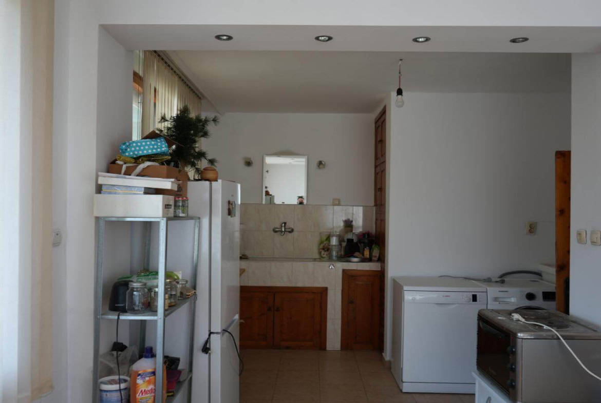 Кухня с бели стени и дървени шкафове, разделена от трапезарията с висок параван.