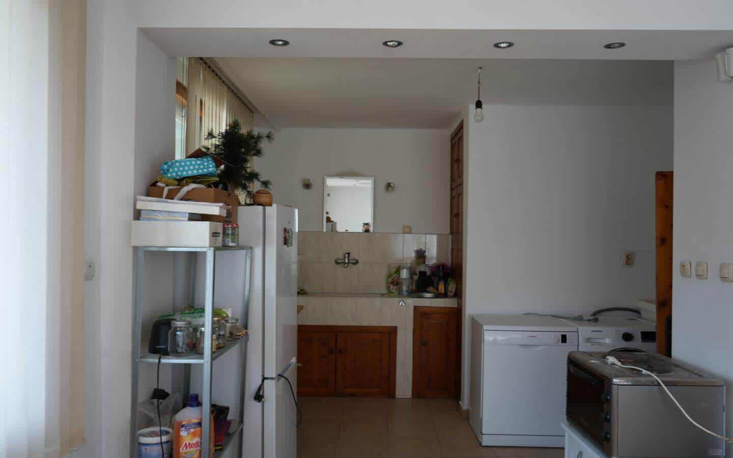 kushta-za-prodajba-kostenec-veranda-8 Кухня с бели стени и дървени шкафове, разделена от трапезарията с висок параван.