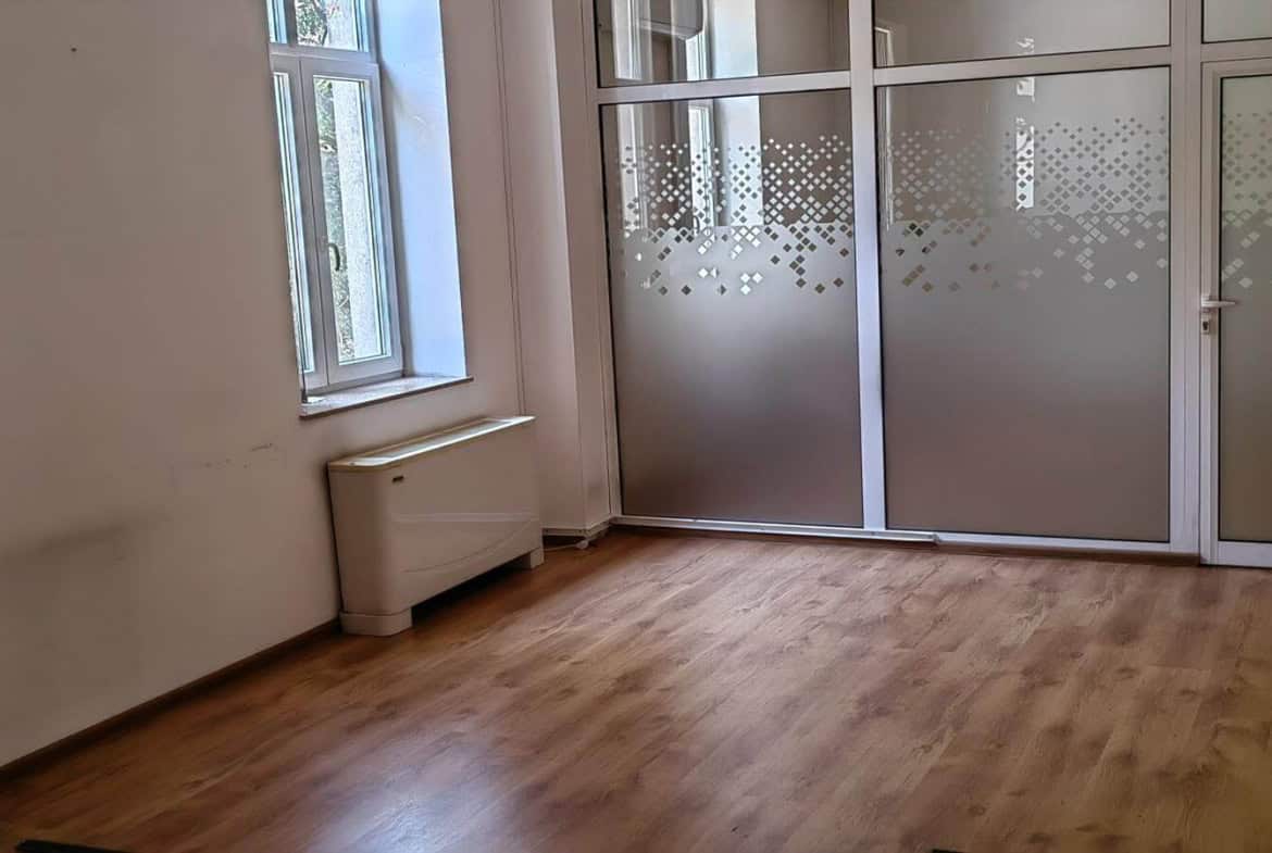 Празна стая с голям прозорец и стъклена врата с матово покритие от офис под наем в София до Централни хали.