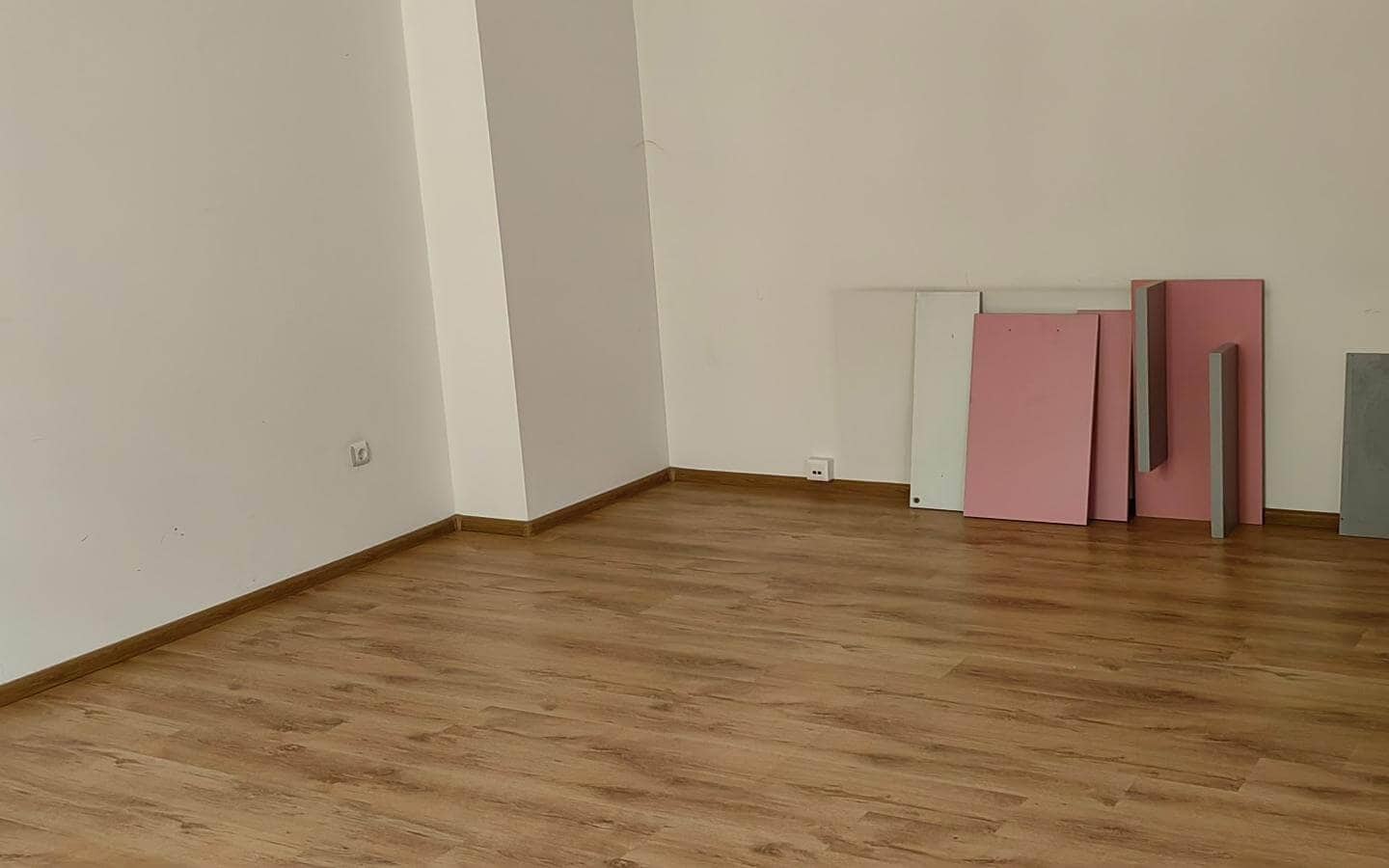 Празна стая с дървен под и няколко цветни плоскости до стената от офис под наем в София до Централни хали.
