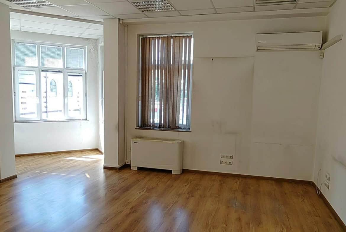 Празна стая с дървен под и прозорец с изглед към улицата от офис под наем в София до Централни хали.