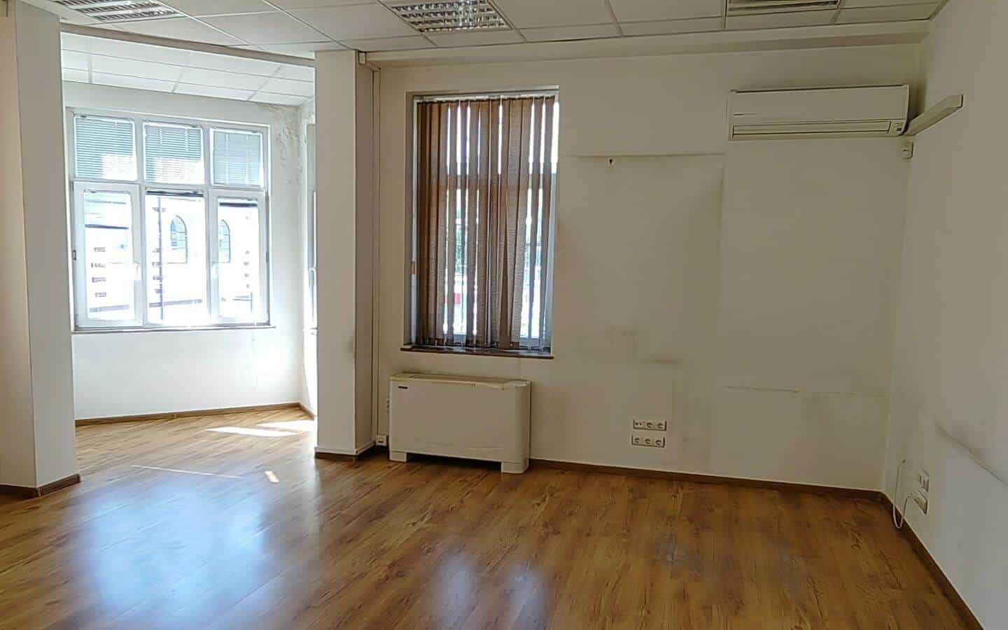 Празна стая с дървен под и прозорец с изглед към улицата от офис под наем в София до Централни хали.