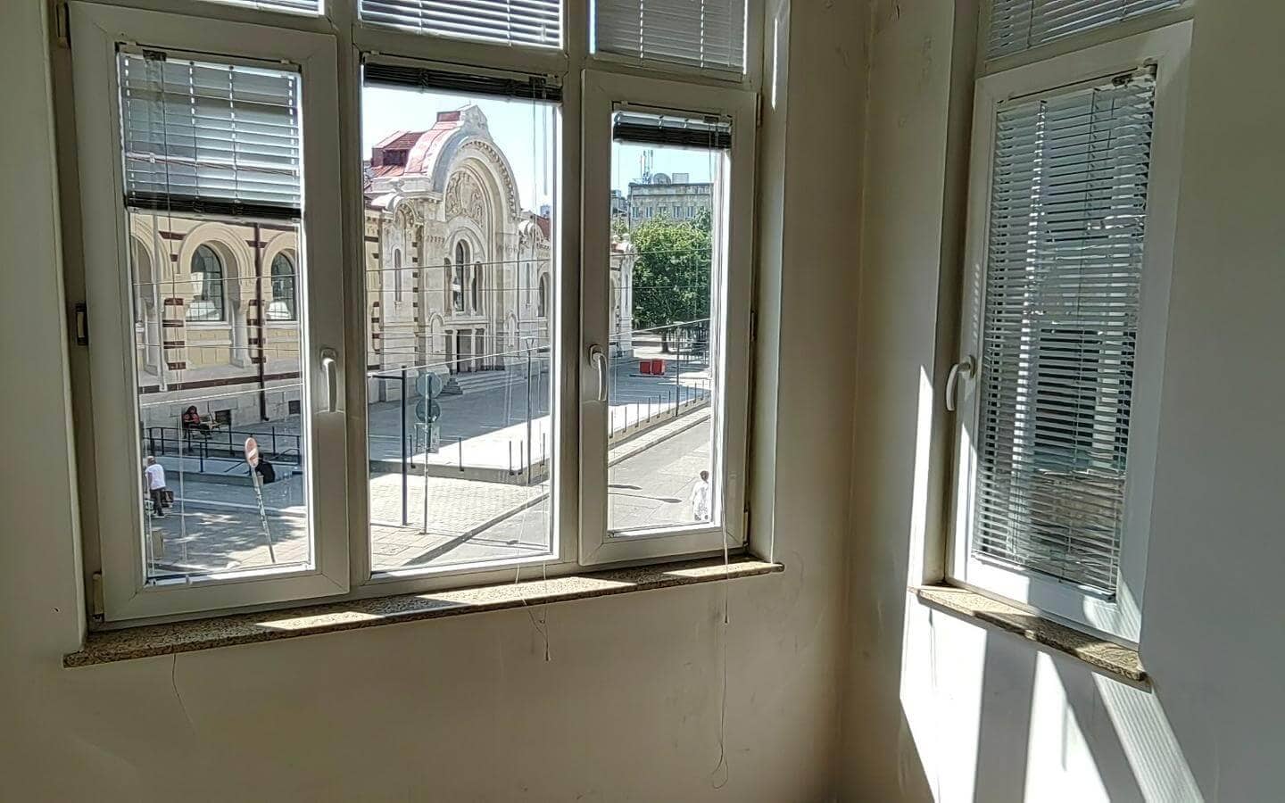Ъгъл на празна стая с прозорци, гледащи към улицата от офис под наем в София до Централни хали.