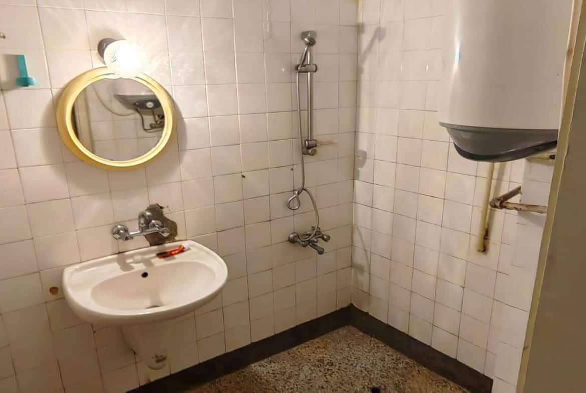 Баня с мивка, душ и бойлер на стената.