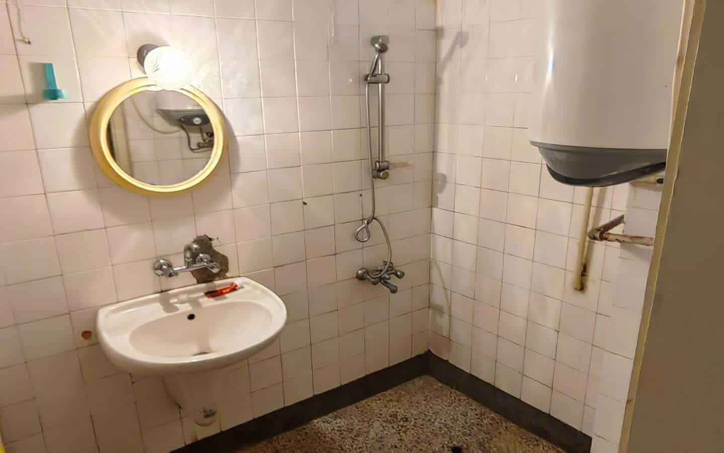 Баня с мивка, душ и бойлер на стената.