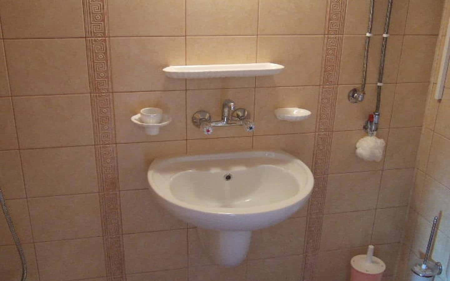 Умивалник с хромирани кранове и огледало, разположени на стена, облицована с кафяви плочки.