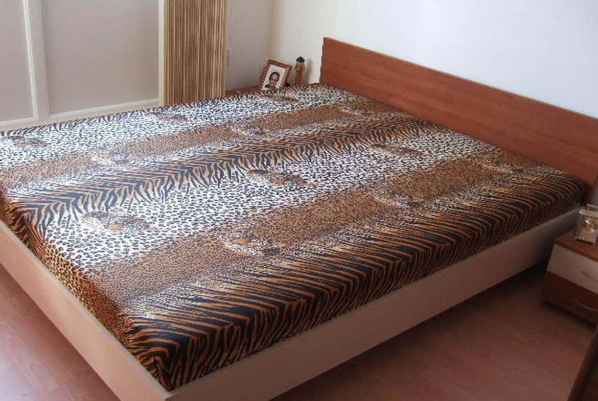 Спалня с голямо легло, покрито с черно-бяло тигрово одеяло, и дървена спалня в светли тонове.