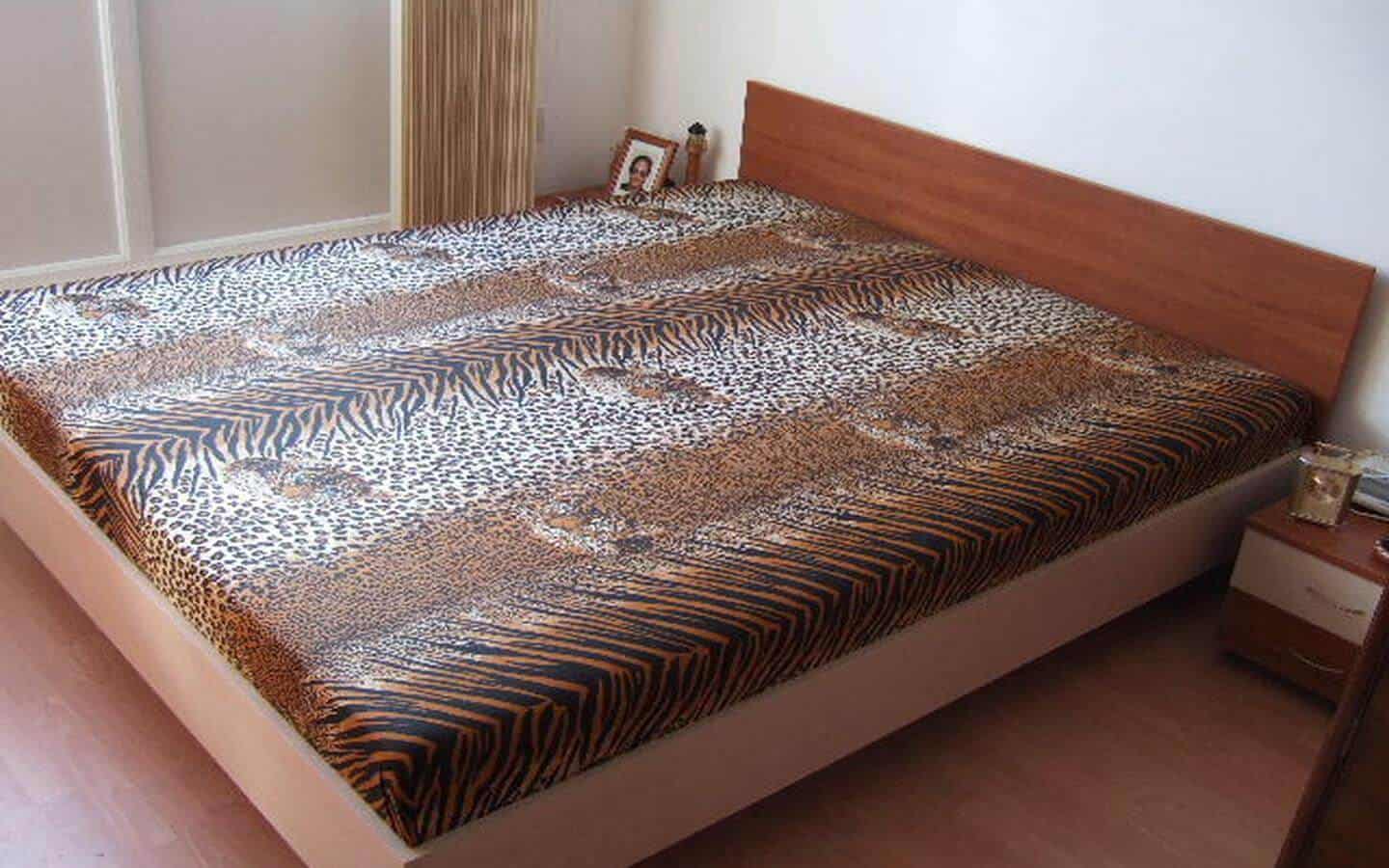 Спалня с голямо легло, покрито с черно-бяло тигрово одеяло, и дървена спалня в светли тонове.