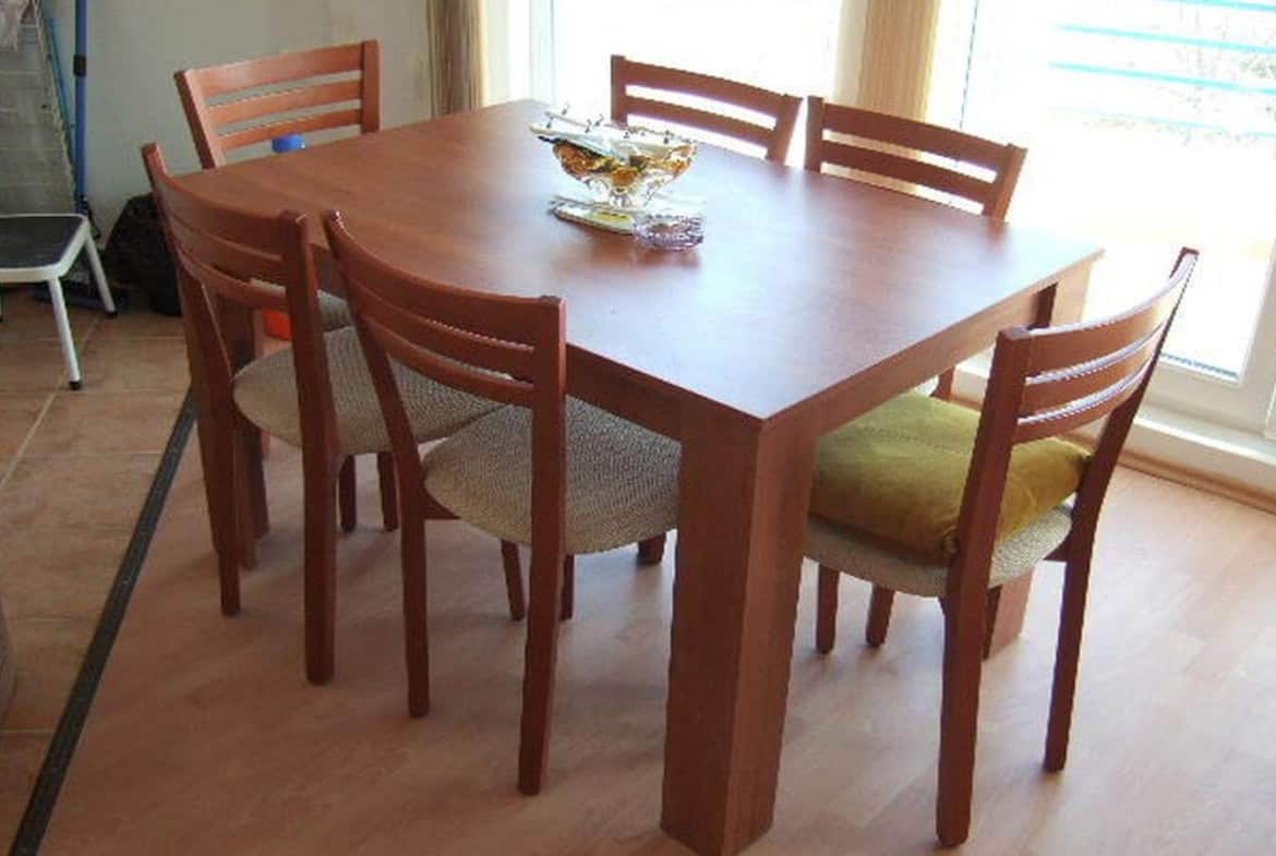 Дървена маса с четири стола около нея, поставени в просторна стая с естествена светлина.