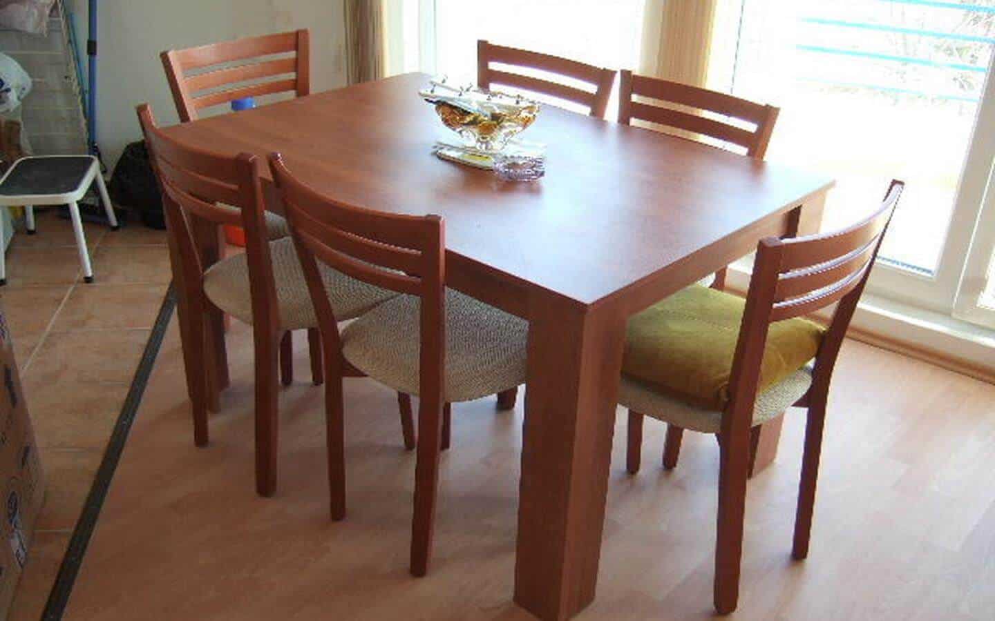 Дървена маса с четири стола около нея, поставени в просторна стая с естествена светлина.