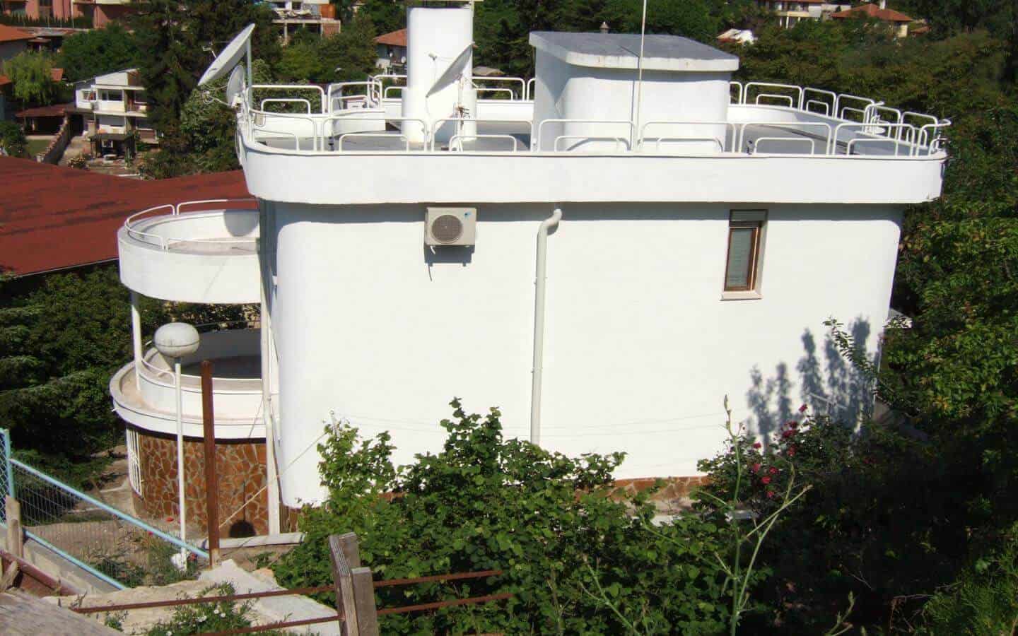 Заснета отгоре кръгла бяла сграда с плосък покрив, заобиколена от балюстради и оборудвана със сателитни антени.